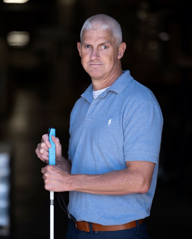 Andy with a serious facing standing and holding his white cane